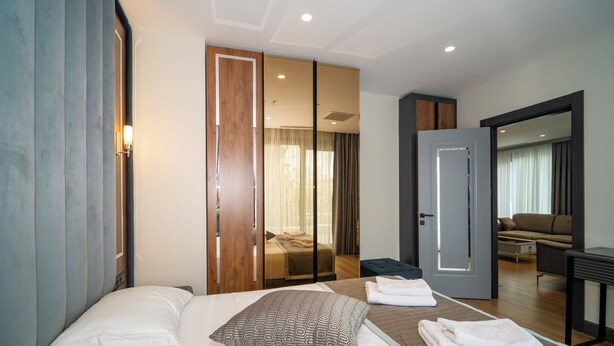 Ein modernes Hotelzimmer mit einem großen Bett, einer separaten Sitzecke und Blick in das Wohnzimmer.