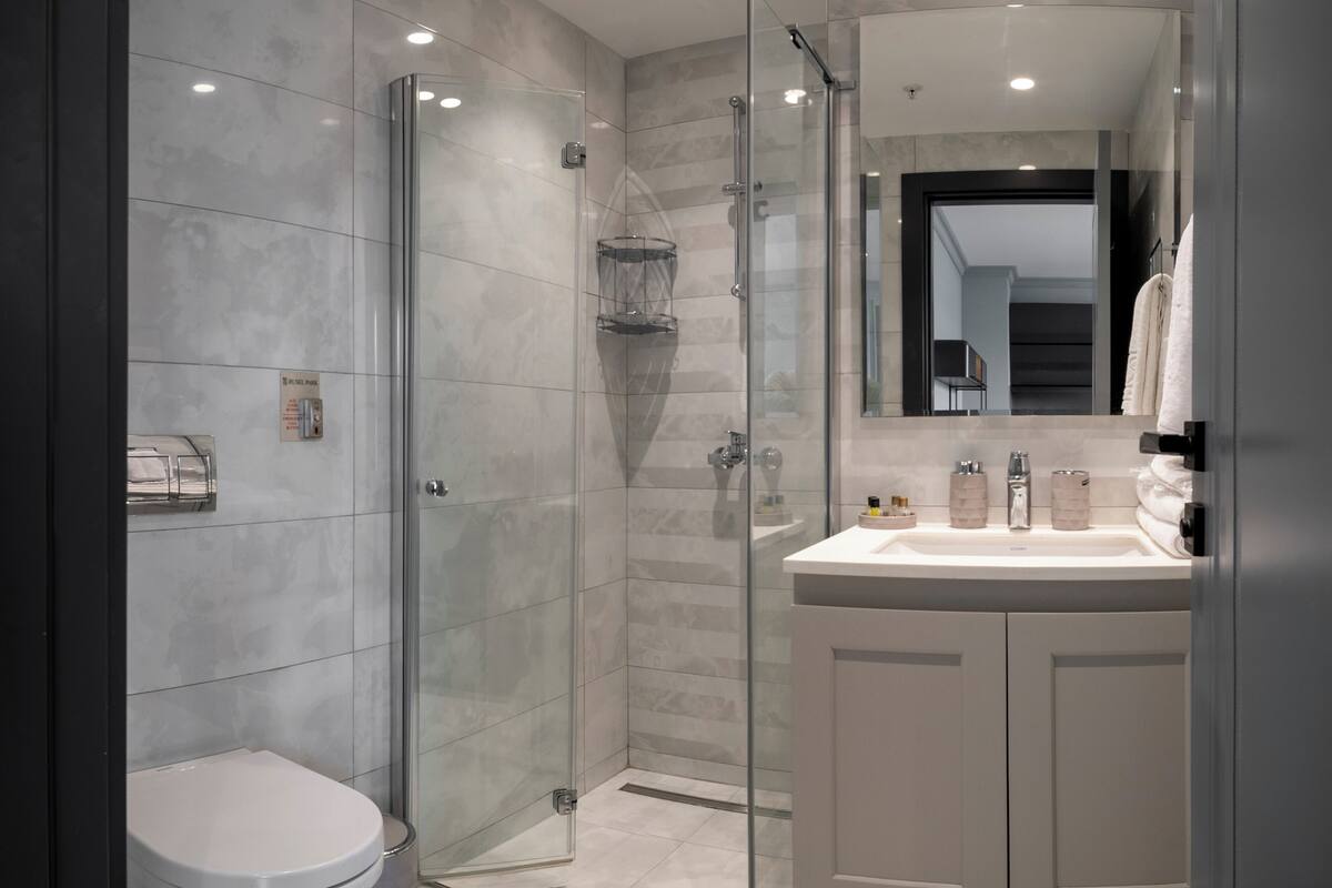 Un baño moderno con ducha de vidrio, inodoro blanco y tocador con espejo.
