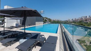 Ein Pool auf dem Dach mit Liegestühlen und Sonnenschirmen mit Blick auf eine Stadtlandschaft.
