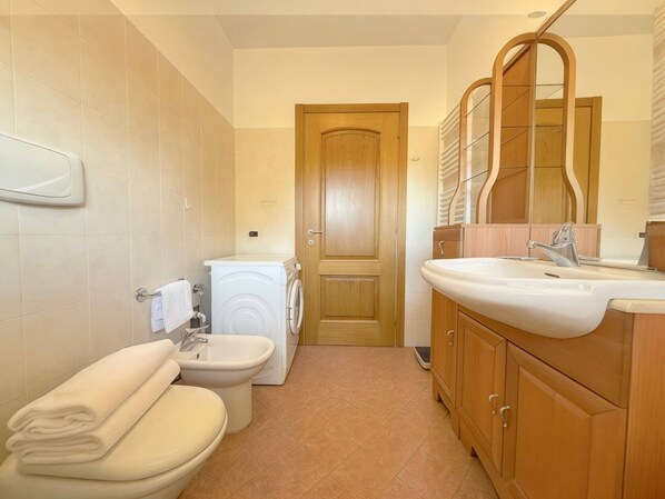 Ein kleines Badezimmer mit Toilette, Bidet, Waschmaschine und Waschbecken mit Spiegel.