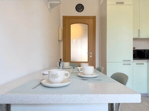 Eine kleine, moderne Küche mit Essbereich. Eine Holztür mit Fensterglas, eine Wanduhr und eine Mikrowelle auf der Arbeitsplatte.