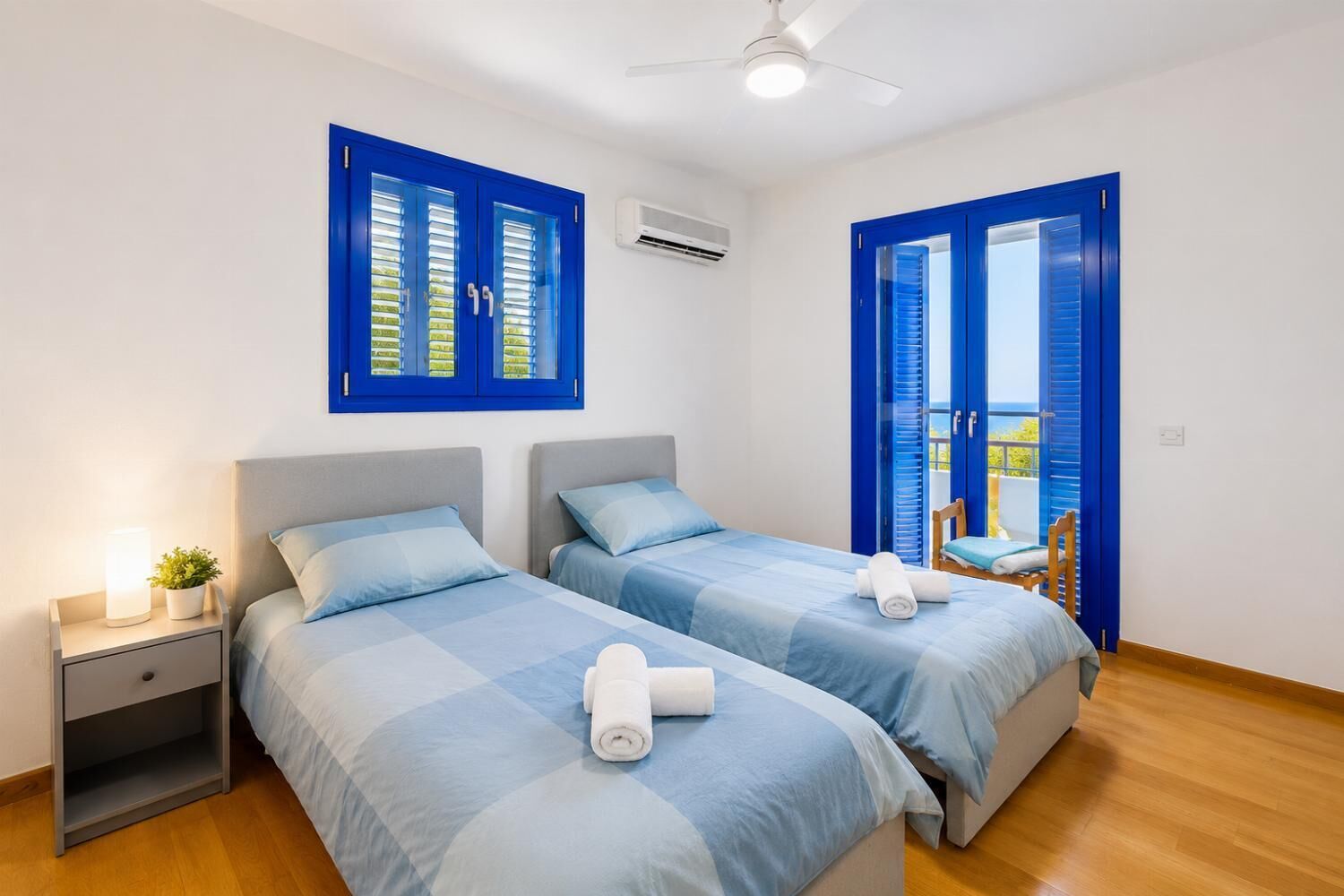 A room with two beds, a nightstand, a ceiling fan, and a view through a door.