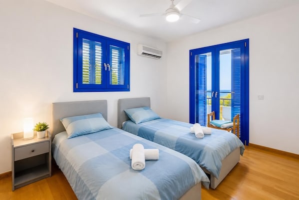 A room with two beds, a nightstand, a ceiling fan, and a view through a door.