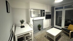 A modern living room with a white fireplace, a dining table, and a sofa with a yellow cushion.