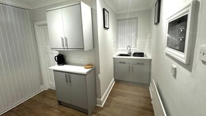 A compact kitchen with white cabinetry, a built-in sink, and a coffee maker.