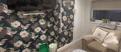 A bedroom with a bed, a sofa, a television on the wall, and a window.