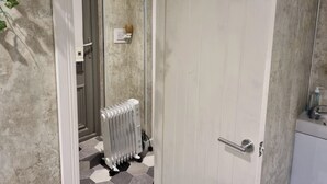 Ett badrum med en vit dörr, ett element och ett kaklat golv.