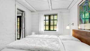Une chambre à coucher avec un grand lit, une fenêtre avec des rideaux, un tableau accroché au mur et une porte donnant sur l’extérieur.