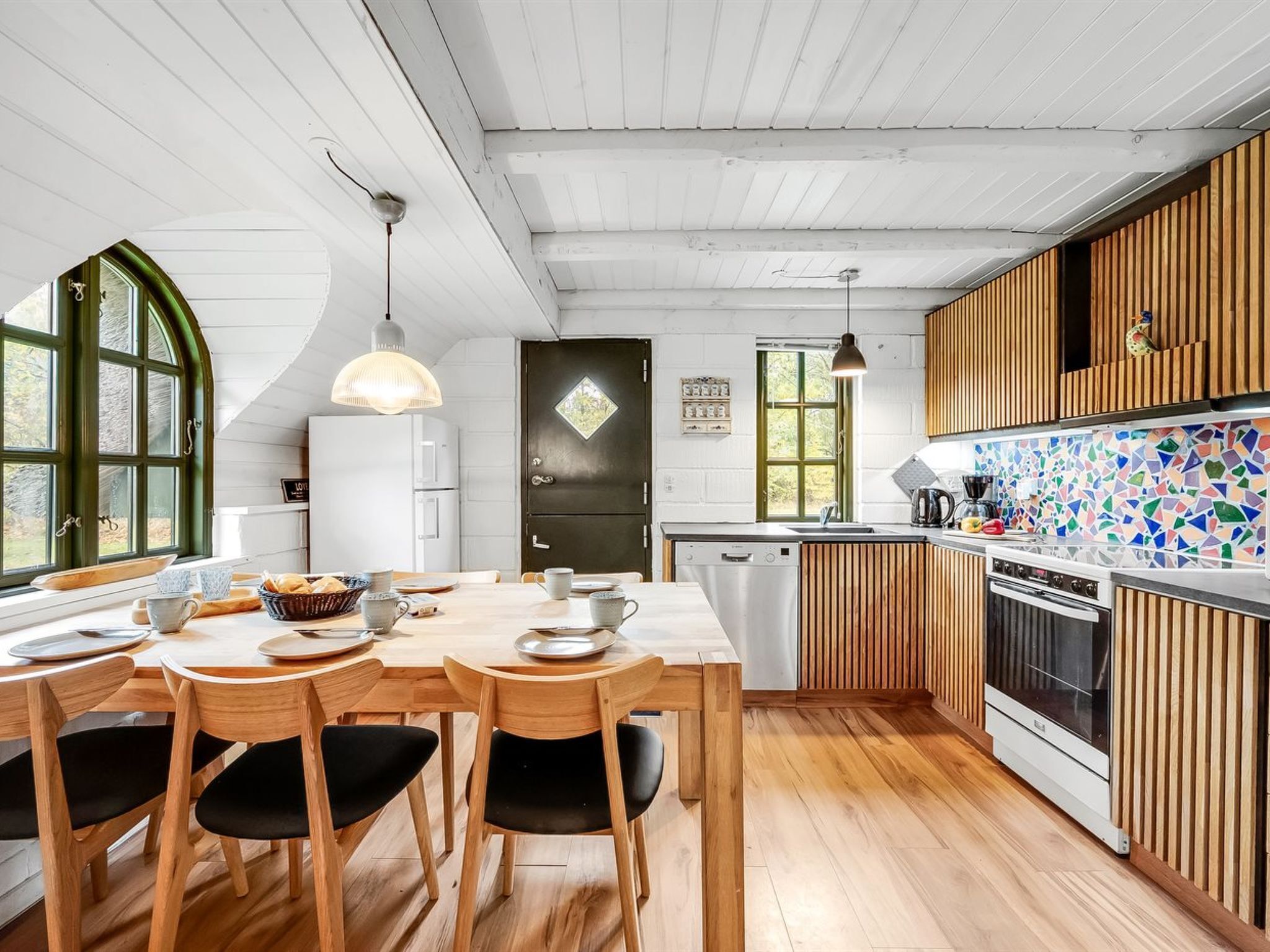 Una cucina moderna con mobili in legno, zoccolo rivestito in piastrelle e zona pranzo con tavolo e sedie in legno.