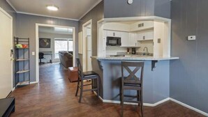 A modern kitchen with a built-in microwave, a coffee maker, and a sink. There are two wooden chairs in front of the counter.