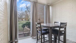 A room with a dining table and chairs, a sliding glass door, and a brick wall.