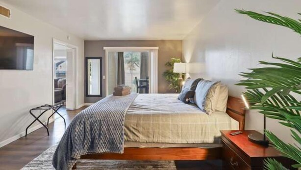 A bedroom with a bed, bedside table, lamp, and a large plant.