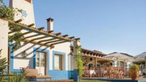 Un bâtiment à la façade bleue et blanche, doté d’une pergola et d’un espace extérieur aménagé pour s’asseoir.