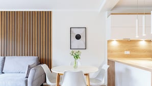 A modern living room with a sofa, dining table, chairs, and a kitchen area with wooden cabinets and pendant lights. - Native Apartments Barska 13 (Kraków)