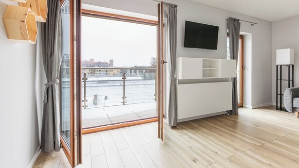 A modern living room with a large sliding glass door leading to a balcony, a flat-screen TV mounted on the wall, and a minimalist furniture arrangement. - Native Apartments Barska 13 (Kraków)