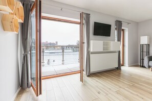 A modern living room with a large sliding glass door leading to a balcony, a flat-screen TV mounted on the wall, and a minimalist furniture arrangement. - Native Apartments Barska 13 (Kraków)