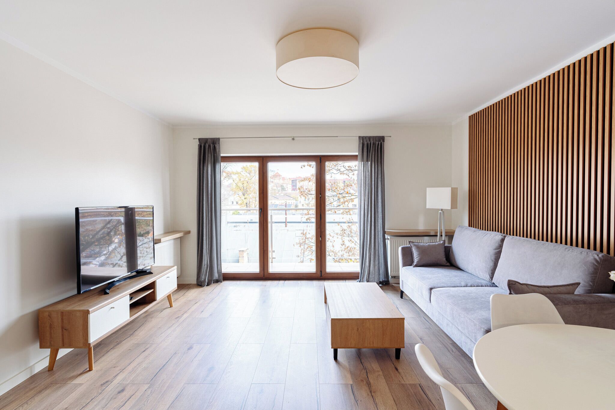 Ein modernes Wohnzimmer mit Flachbildfernseher, einer Couch, einem Couchtisch und einem Esstisch.