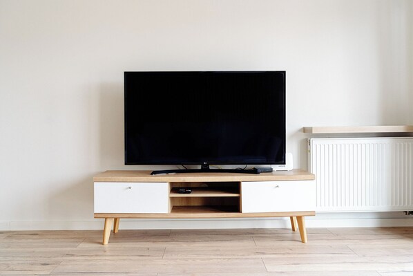A modern entertainment unit with a flat-screen TV, wooden drawers, and a shelf. - Native Apartments Barska 13 (Kraków)