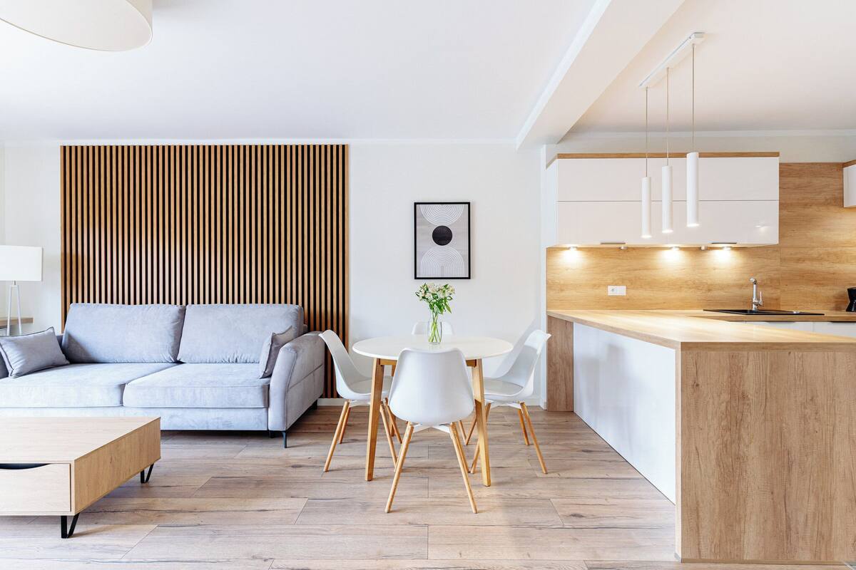 Un salon moderne comprenant un canapé, une table à manger et des chaises, un coin cuisine avec des meubles en bois et un mur avec des lambris en bois.