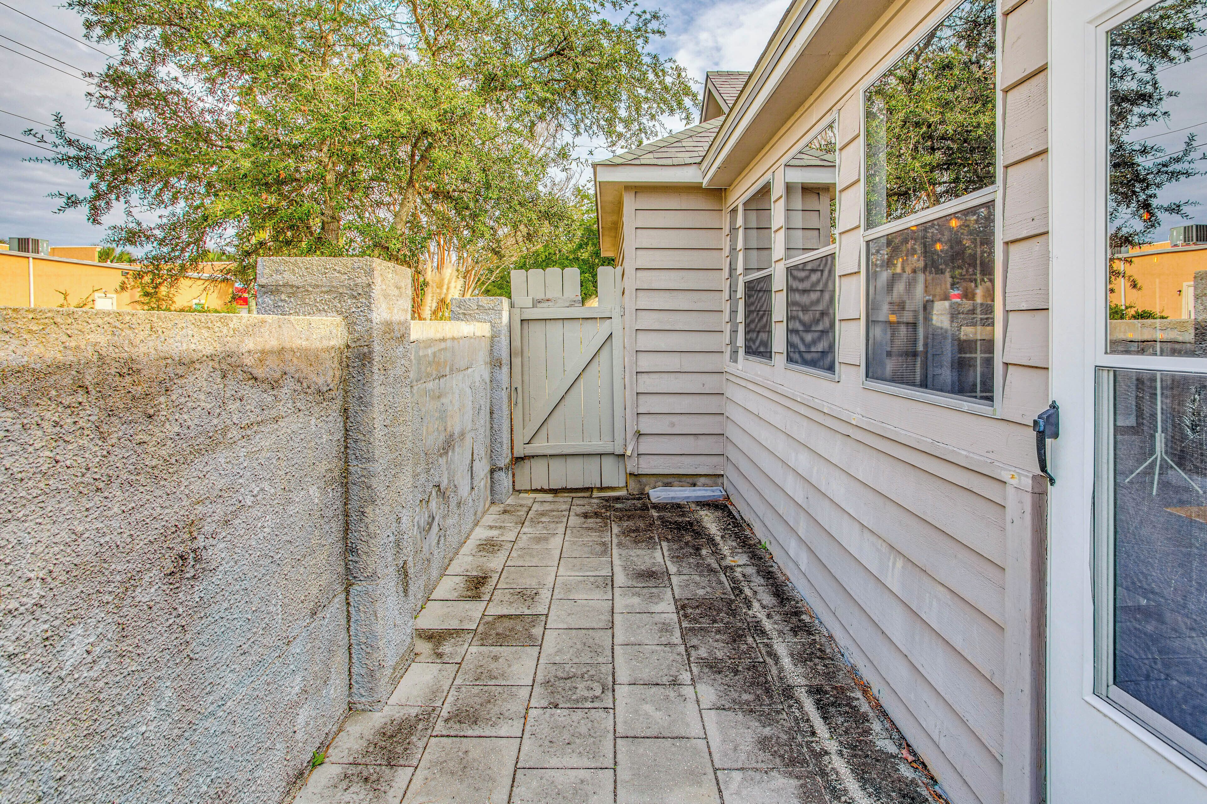 A narrow concrete pathway leading to a house with a wooden fence and a window with a screen.