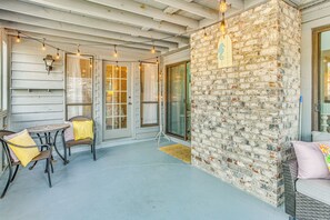 A covered patio with a brick wall, wicker furniture, and string lights. - Cozy North Myrtle Beach Home: 3 Blocks to Ocean! (North Myrtle Beach)