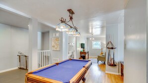 Ein geräumiger Raum mit Poolbillard, Holzboden, einer Treppe und einem Chandelier.