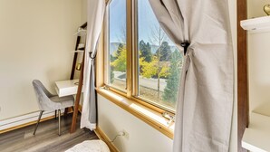 A room with a large window, a white desk, a grey chair, and a white shelf. - Condo w/ Balcony > 2 Mi to Angel Fire Resort! (Angel Fire)