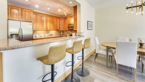 A modern kitchen with wooden cabinets, a stainless steel refrigerator, and a bar area with stools. - Condo w/ Balcony > 2 Mi to Angel Fire Resort! (Angel Fire)
