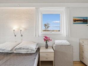 Une chambre à coucher avec un lit, des lampes de chevet, une table de chevet, une commode, une fenêtre donnant sur un beau paysage et un tableau accroché au mur.