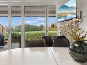 Een vergaderruimte met een grote tafel, stoelen, een televisiescherm en uitzicht op een bergachtig landschap door grote glazen deuren.