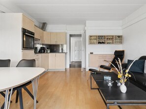 Een moderne keuken met houten kastjes, een ingebouwde oven en een eethoek met een witte tafel en stoelen.