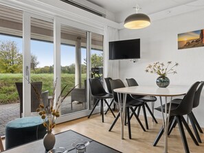 Un espace de salle à manger moderne avec une table ronde, des chaises noires et une grande fenêtre donnant sur l’extérieur.