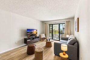 Una sala de estar moderna con un televisor de pantalla plana, un sofá, una mesa de centro y una pequeña mesa redonda con una lámpara.