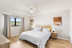 A bedroom with a bed, nightstands, a ceiling fan, a window with curtains, and artwork on the walls.