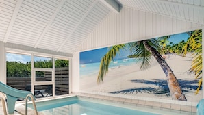 An indoor swimming pool with a slide, a beach mural, and a view of the sea.