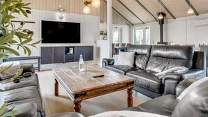 A spacious living room with a large leather sofa, a wooden coffee table, and a flat-screen TV mounted on the wall.