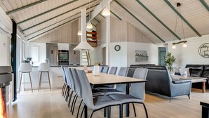 A spacious dining area with a long table and multiple chairs, a cozy seating area with a sofa, and a kitchen in the background.