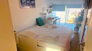 A bedroom with a bed, a nightstand, a desk, a chair, and a potted plant.