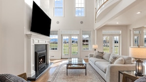 A spacious living room with a fireplace, a sofa, a coffee table, and a television mounted on the wall.