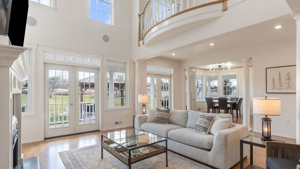 A spacious living room with a high ceiling, a staircase, and large windows.