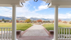 A covered porch with white columns, a brick pathway, and a view of mountains and autumn trees.