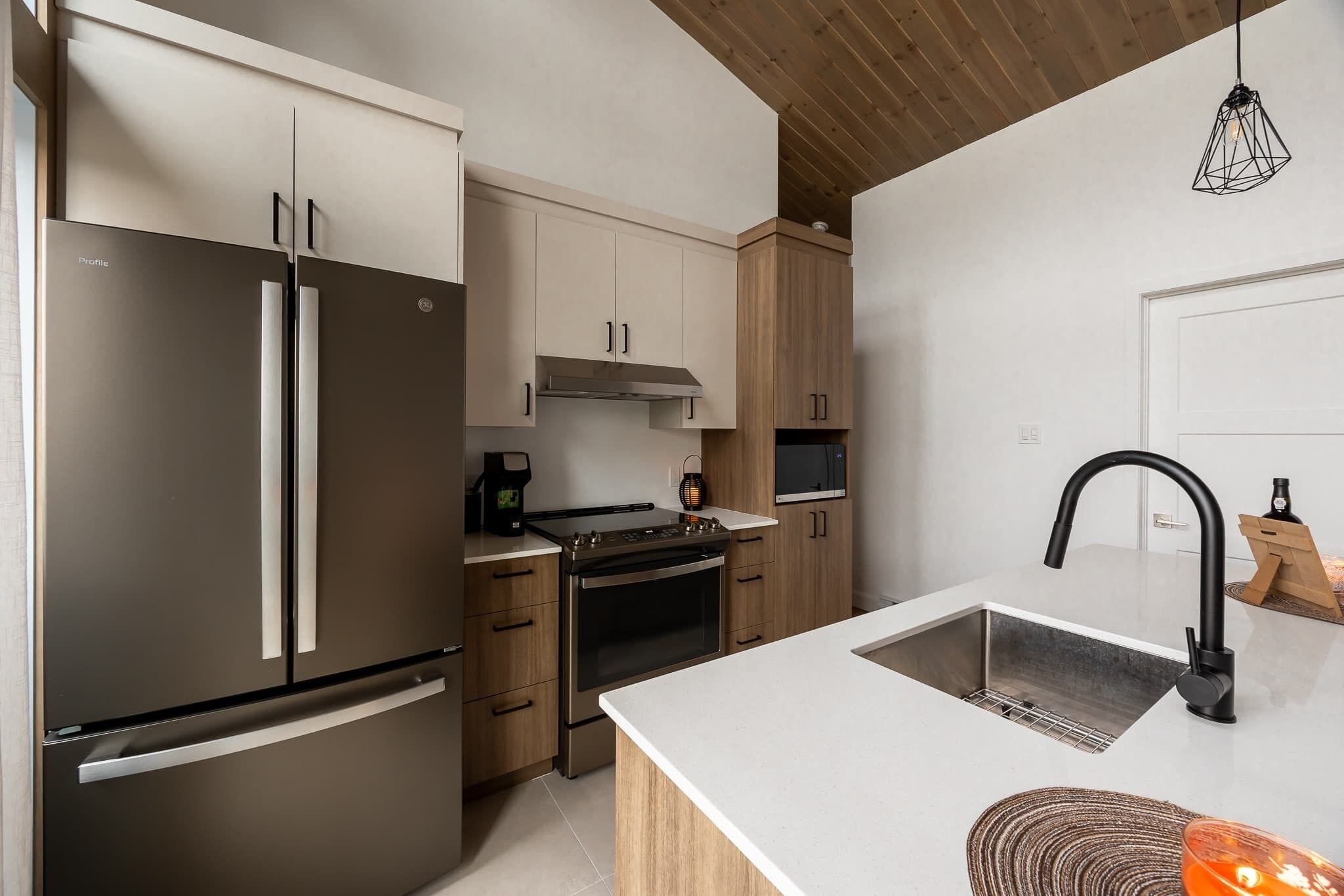 Una cocina moderna con refrigerador de acero inoxidable, armarios de madera, horno empotrado y encimera blanca.