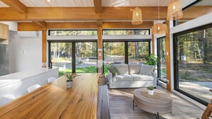 Une cuisine moderne avec un plan de travail en bois et des chaises blanches, un coin repas avec une table et des chaises en bois, et un espace détente avec un canapé et une table basse.