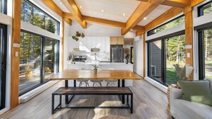 Une cuisine moderne dotée de grandes fenêtres, un coin repas avec une table et des bancs en bois, et une vue sur l’extérieur.