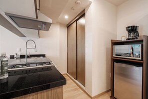 Une cuisine compacte dotée d’un plan de travail noir, d’appareils électroménagers en acier inoxydable et d’une armoire à portes coulissantes en bois.