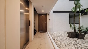 A hallway with a marble floor, a wooden door marked '100', and potted plants. - Stylish 2BR on Reforma · Near Revolución (Mexico City)