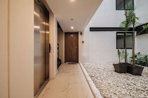 Un couloir doté d’un sol en marbre, d’une porte en bois portant l’inscription « 100 » et de plantes en pot.