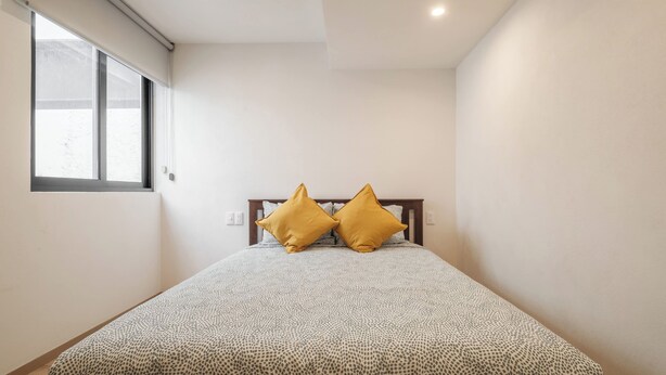 A bedroom with a bed, two pillows, a window, and a ceiling light. - Stylish 2BR on Reforma · Near Revolución (Mexico City)