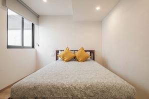 Une chambre à coucher avec un lit, deux oreillers, une fenêtre et un luminaire au plafond.