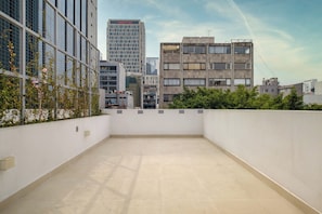 Une terrasse sur le toit offrant une vue sur les bâtiments environnants, notamment un grand immeuble de bureaux et un immeuble résidentiel plus petit.